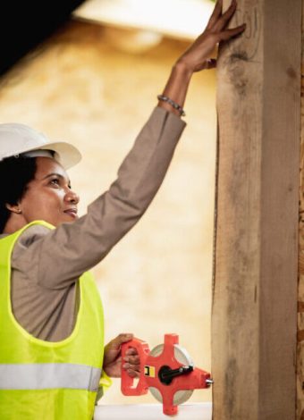 Shot of an African American female architect measuring a window while checking construction site of a new wooden house.